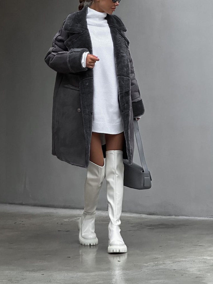 Person wearing a long dark coat, white turtleneck, white knee-high boots, and holding a black handbag against a gray background.