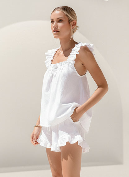 Woman wearing a white dress with ruffled details against a plain background
