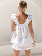Woman wearing a white ruffled top and shorts against a plain background