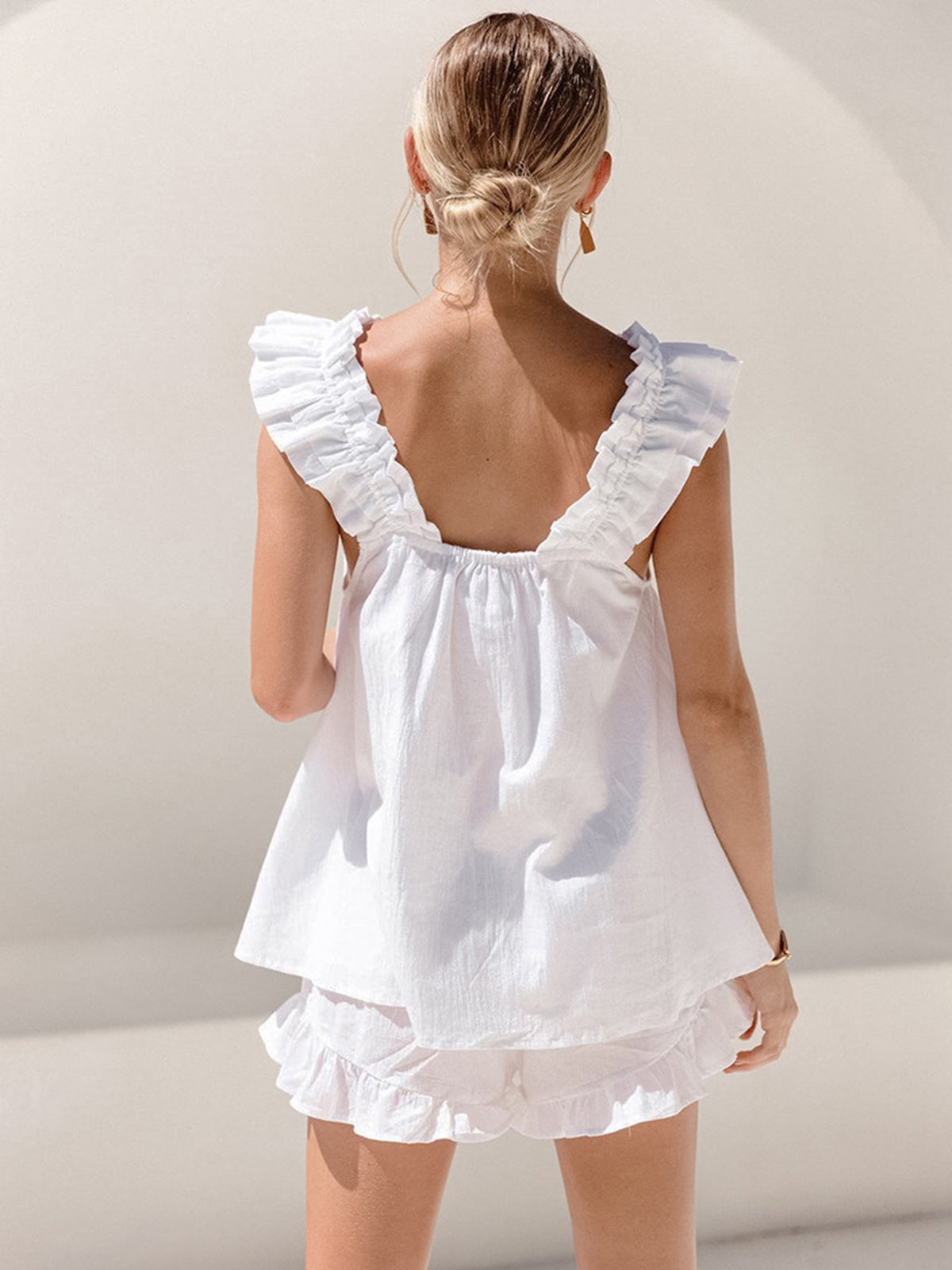 Woman wearing a white ruffled top and shorts against a plain background