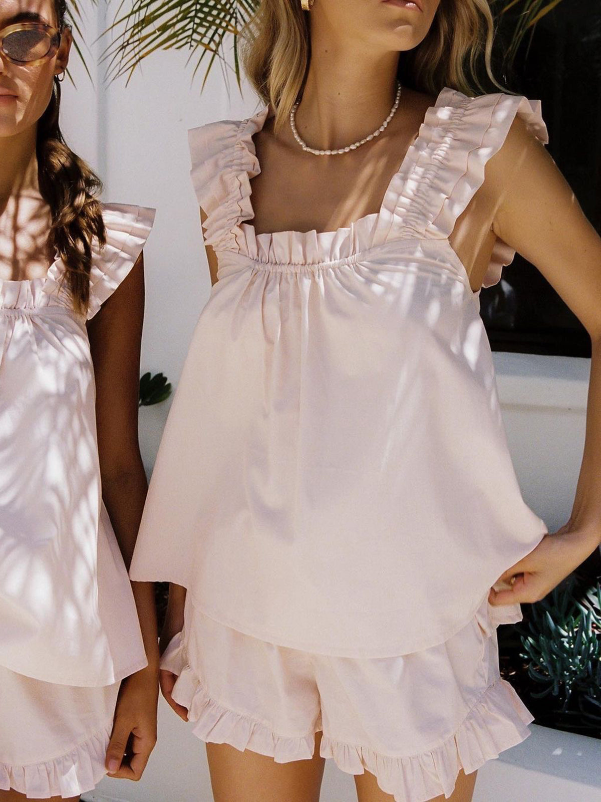 Two women wearing matching light pink outfits with ruffled details.