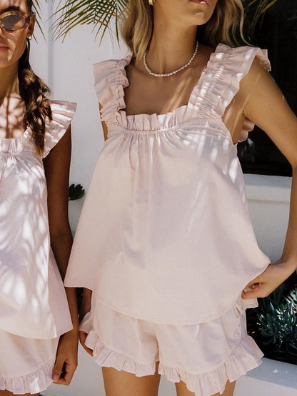 Two women wearing matching light pink outfits with ruffled details.