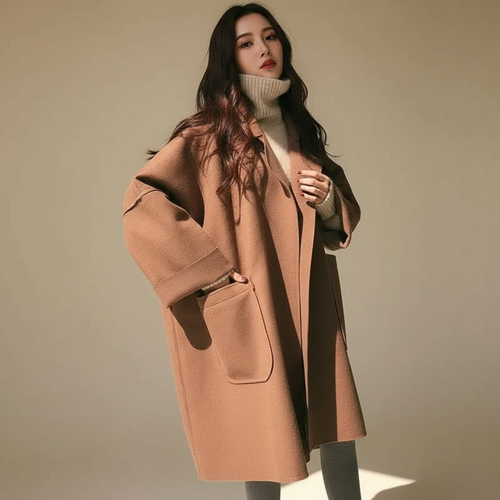 Person wearing a long brown coat in a minimal indoor setting