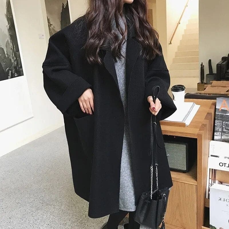 Person wearing a long black coat in an indoor setting