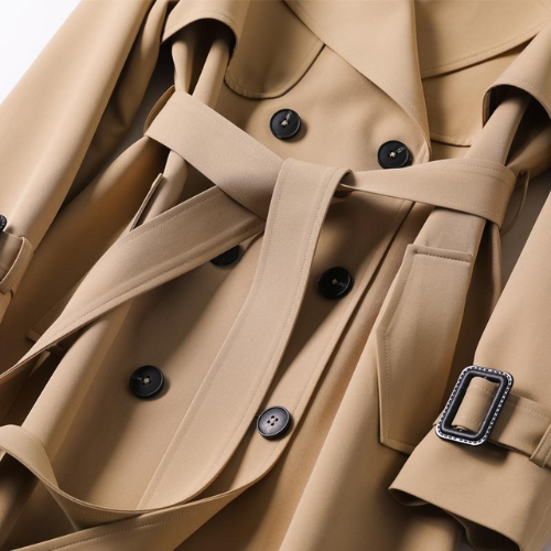 Close-up of a beige trench coat with black buttons and a belt buckle.
