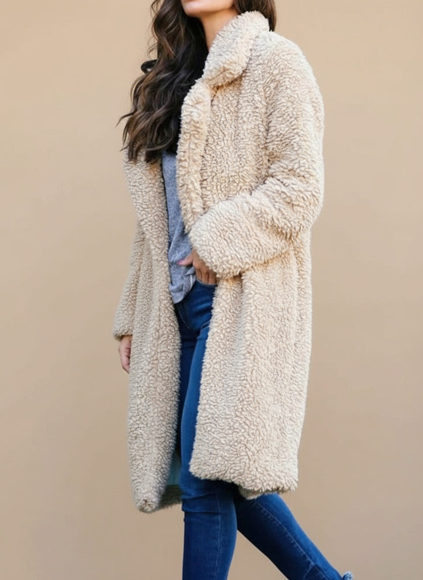 Person wearing a beige teddy coat holding a drink and a black bag outdoors.