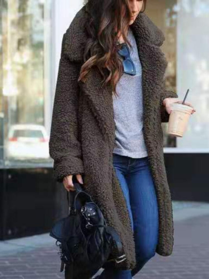 Person wearing a brown teddy coat holding a coffee cup and black bag on a city street.