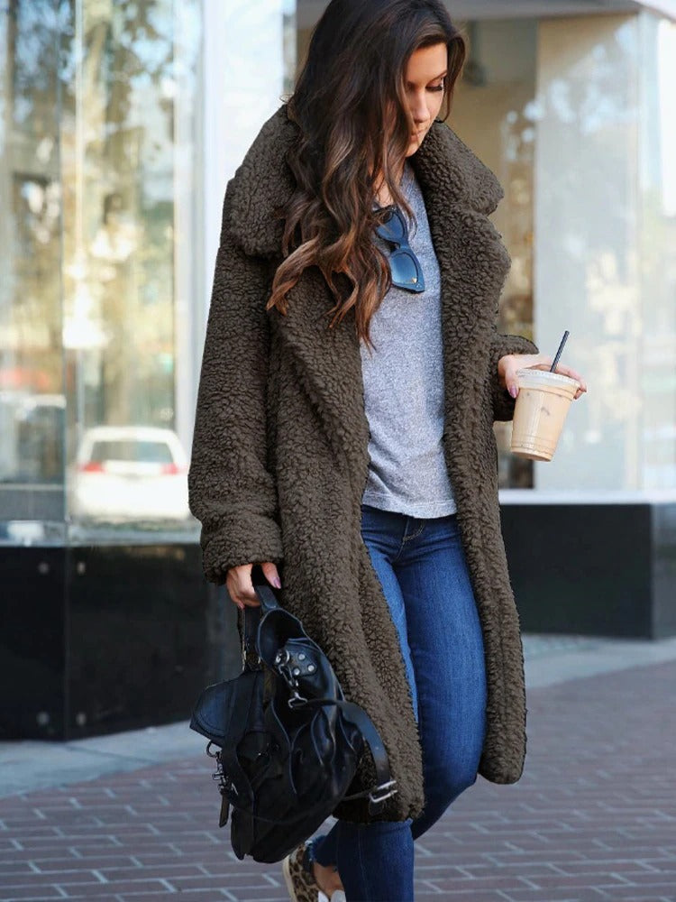 Woman wearing a brown teddy coat holding a coffee cup and black backpack on a city street.